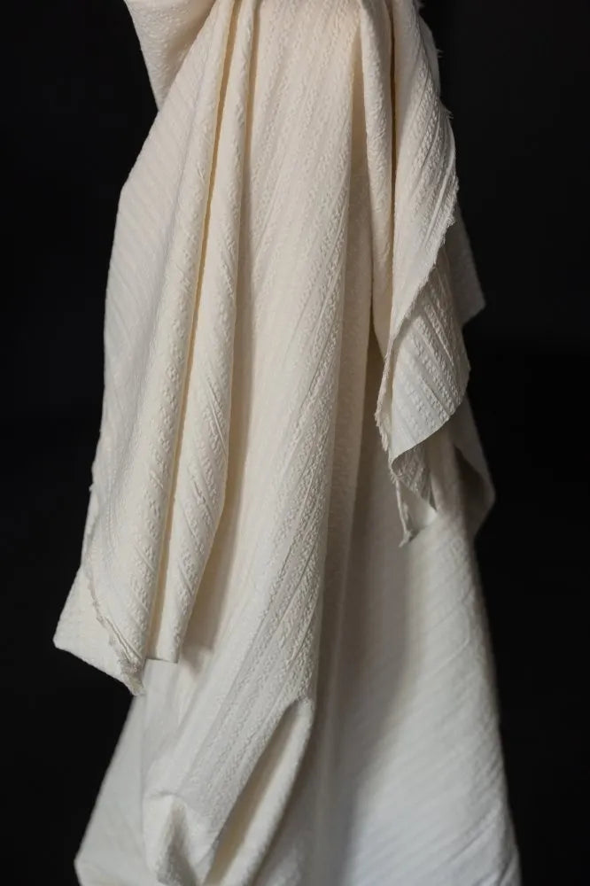 A close-up of draped off-white textured fabric with a crinkled,linen, shown against a solid black background.