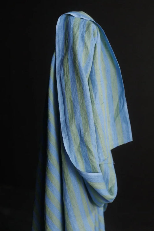A draped light blue and pale yellow striped fabric garment, shown hanging against a solid black background.