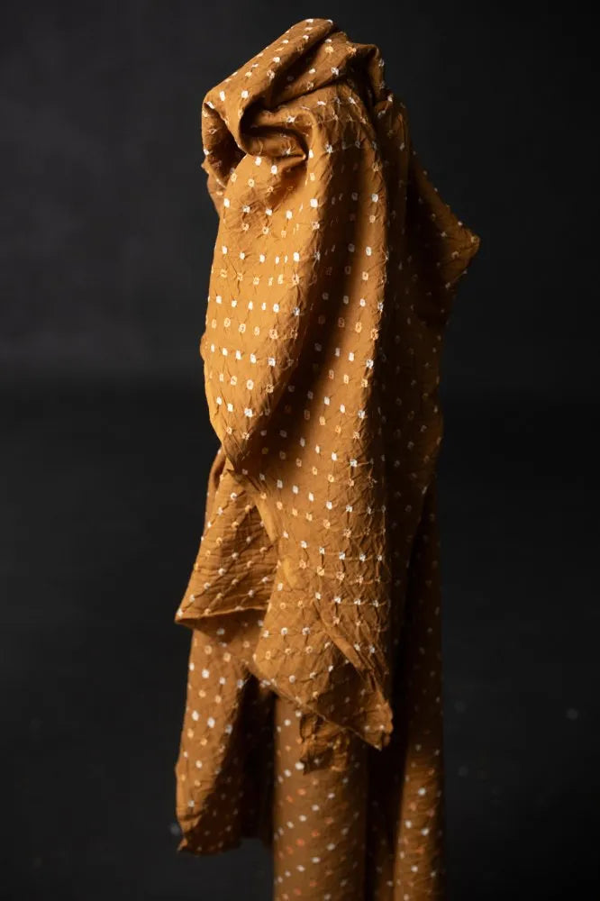 A draped piece of rust-brown fabric with a white dotted pattern, shown against a dark black background.