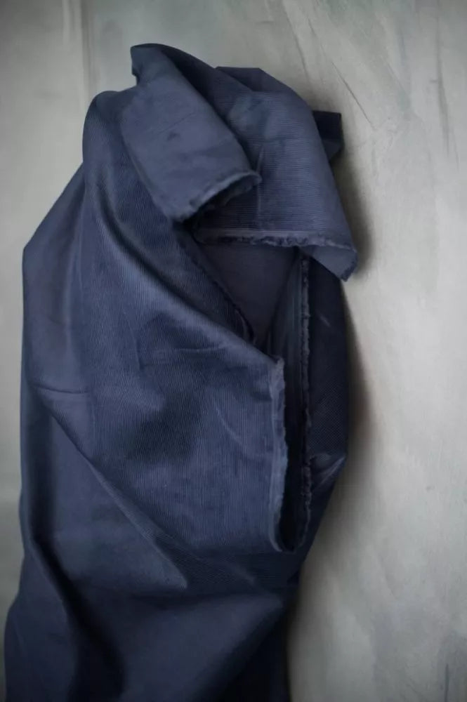 A folded piece of dark navy blue fabric, likely cotton or linen, draped on a textured light gray surface.