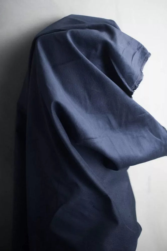 A dark navy blue fabric garment, likely a shirt or blouse, draped and hanging against a plain off-white wall.