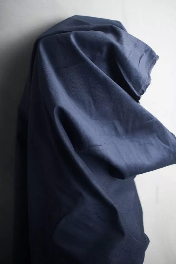 A dark navy blue fabric garment, likely a shirt or blouse, draped and hanging against a plain off-white wall.