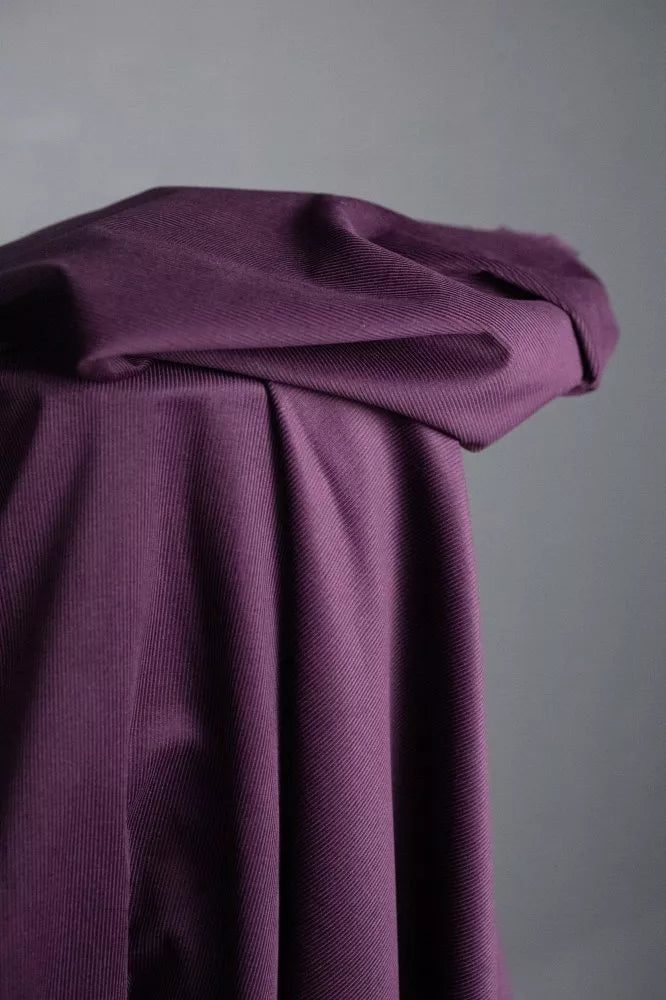 A draped piece of textured purple fabric, folded and gathered against a neutral gray background.