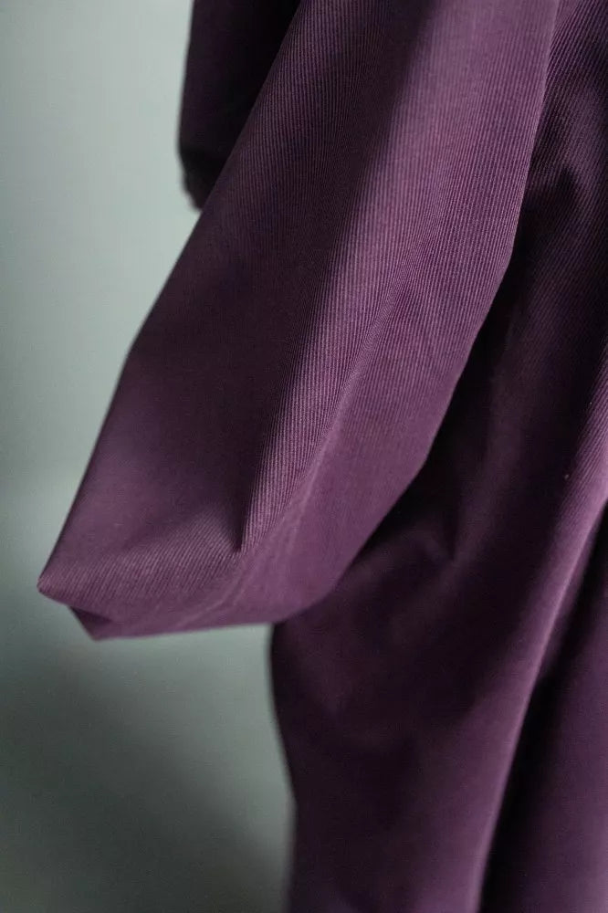 A close-up of a draped purple garment, showing the fabric texture and folds against a soft gray background.