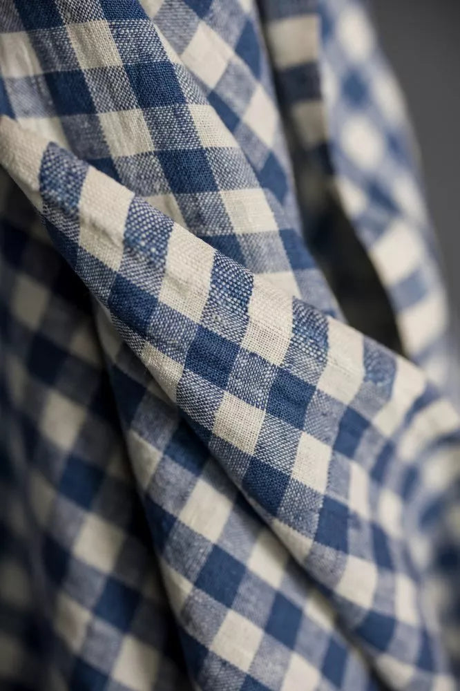 A close-up of blue and off-white gingham fabric draped in soft folds, showing the woven texture and check pattern.