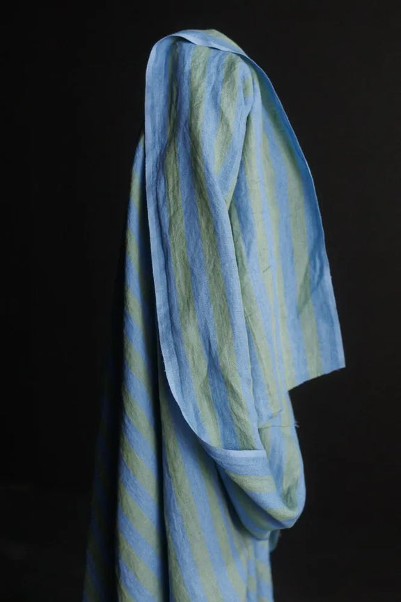 A draped light blue and pale yellow striped fabric garment, shown hanging against a solid black background.