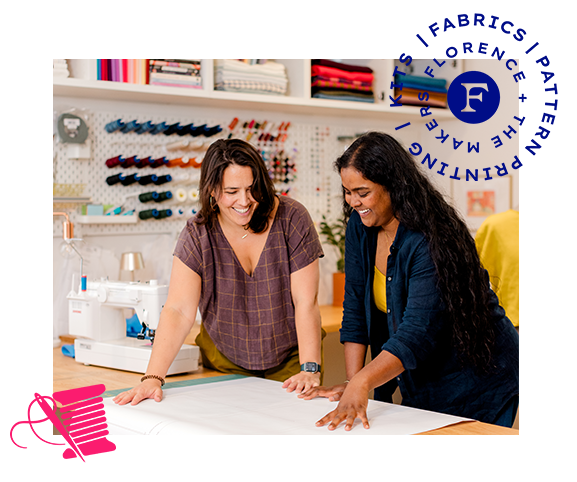 Two women collaborating in a sewing room, looking at a large sheet of white fabric on a table. A white sewing machine is visible in the background, along with shelves of thread and fabric spools.