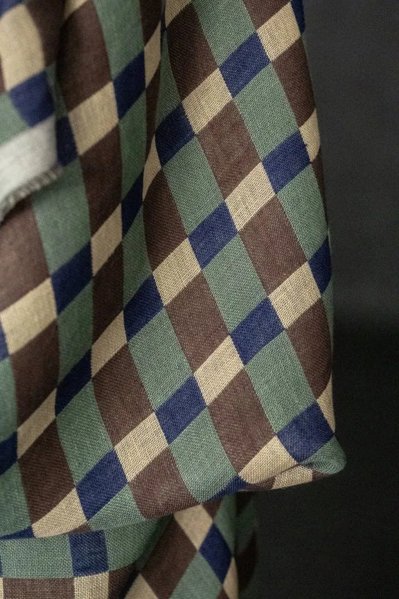 A close-up of a woven textile with a repeating diamond pattern in muted green, brown, navy blue, and cream, draped against a dark background.